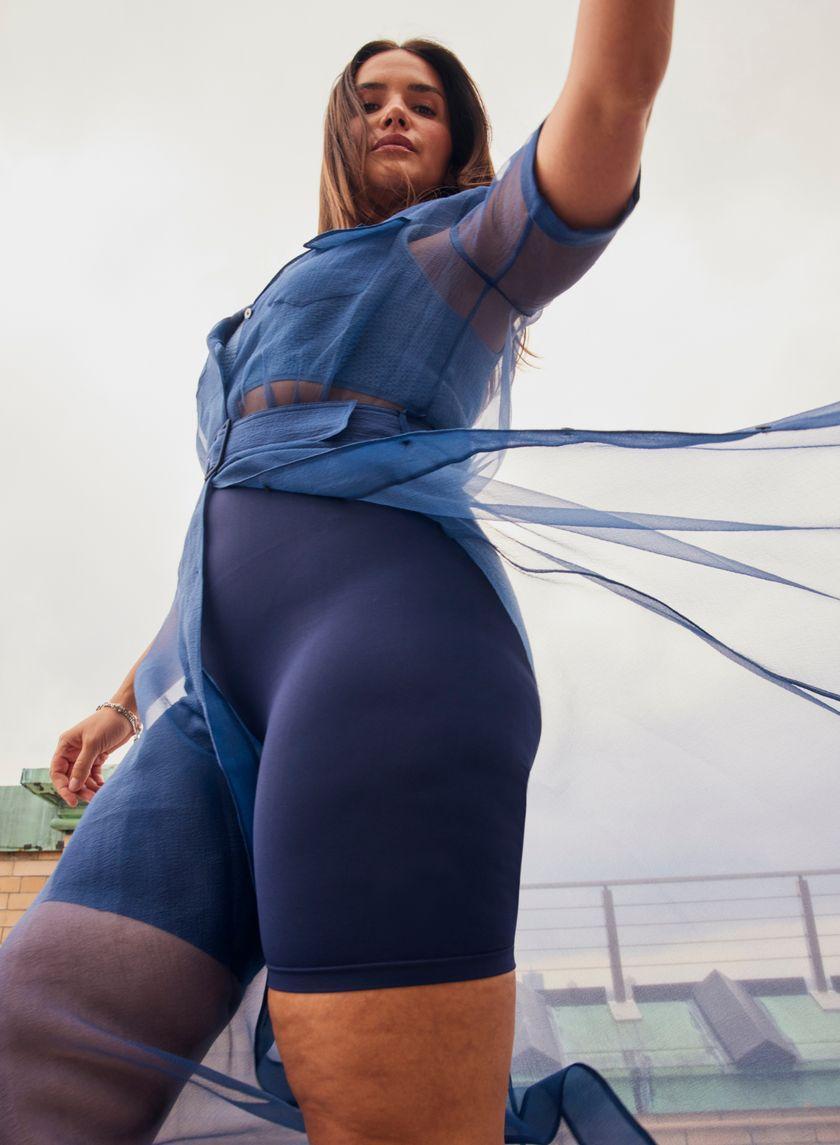 A below view of a woman moving  in blue slip shorts layered under a sheer dress